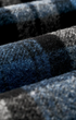 Close-up of a textured wool fabric with a dark blue, black, and gray plaid pattern.