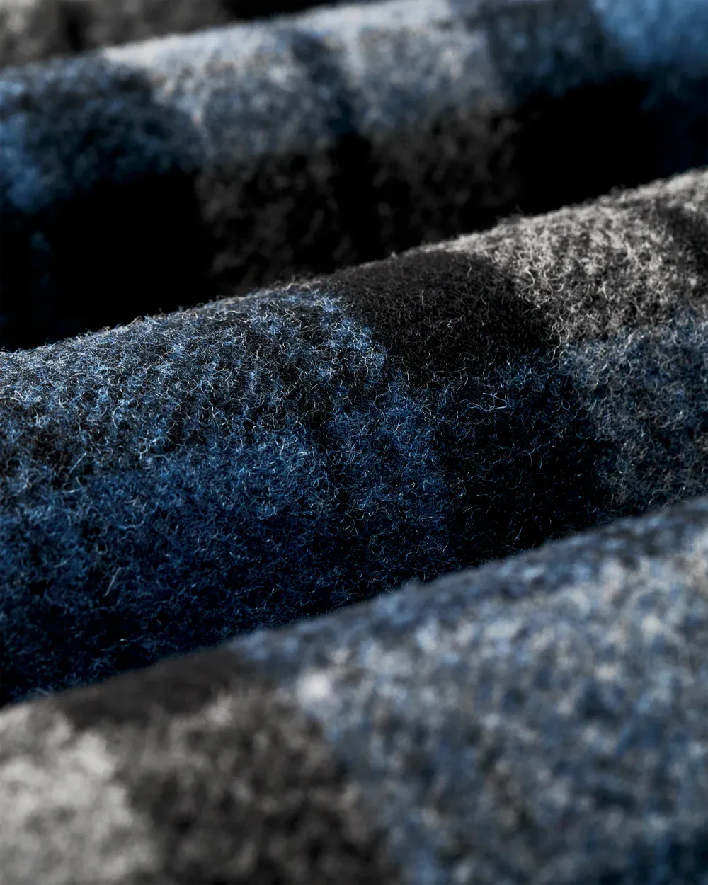 Close-up of a textured wool fabric with a dark blue, black, and gray plaid pattern.