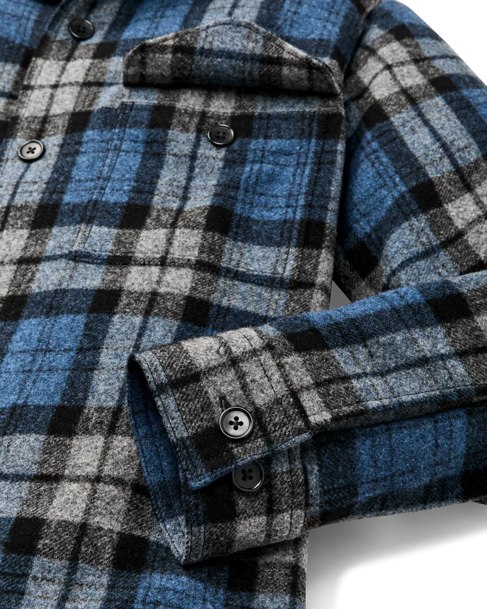 Close-up of a blue, black, and gray plaid flannel shirt with a buttoned chest pocket and folded cuff showing dark buttons.