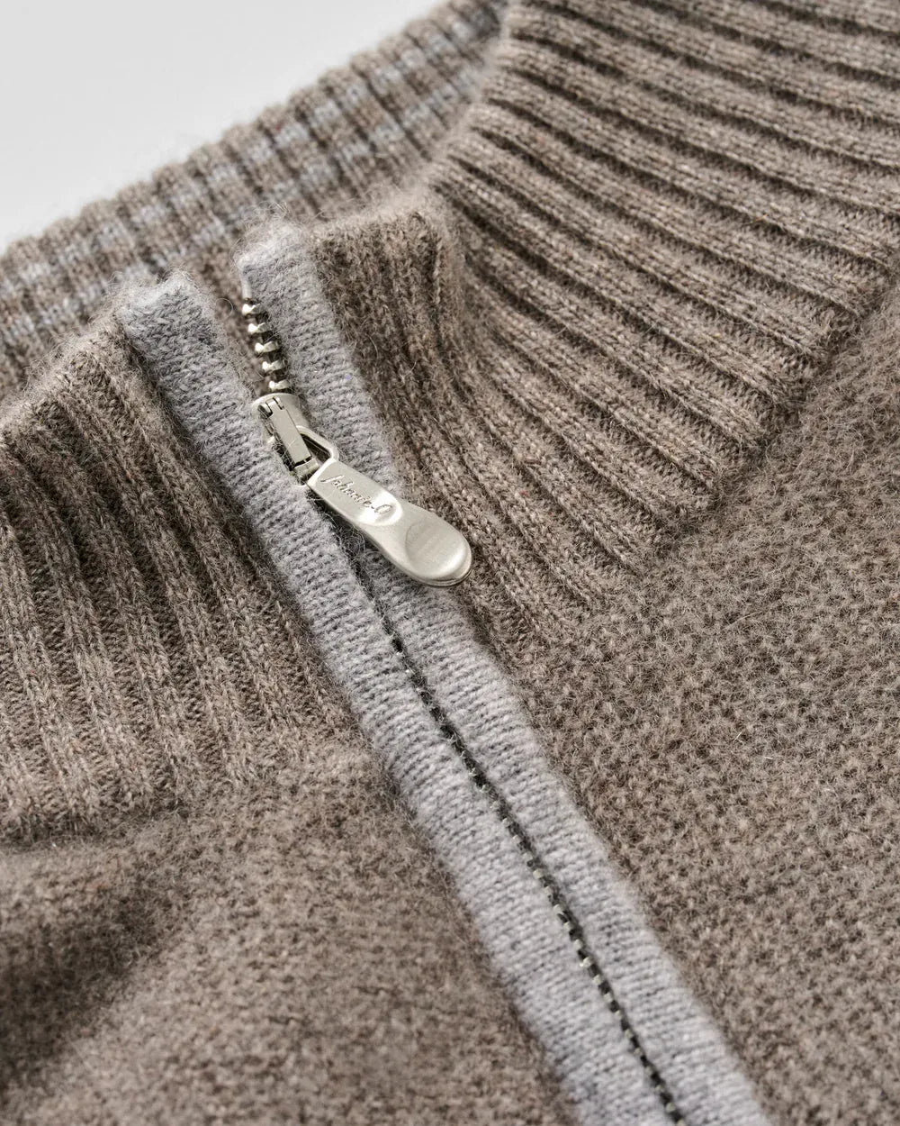 Close-up of a ribbed knit sweater with a silver zipper and pull tab, showing the texture and color of the fabric in detail.
