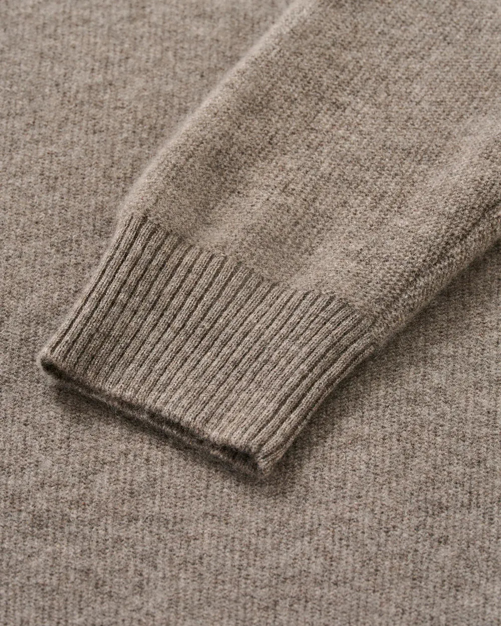 Close-up of a ribbed knit sweater cuff in a warm taupe-beige color, showing the texture and stitching detail.