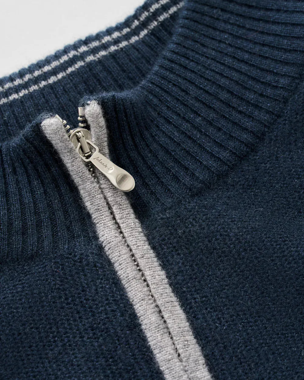 Close-up of a navy blue ribbed knit sweater with a silver zipper and a light gray stripe running down the front.