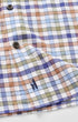 Close-up of a plaid button-up shirt with a multicolor check pattern in blue, purple, green, and peach on a white base, featuring a small embroidered polo player logo near the cuff.
