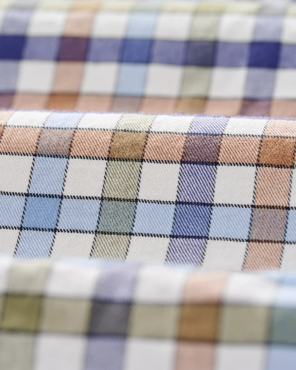 A close-up of folded plaid fabric with a multicolor check pattern featuring white, blue, purple, beige, and brown tones.