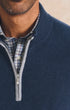 Close-up of a man wearing a navy blue quarter-zip knit sweater over a blue and white plaid button-down shirt.