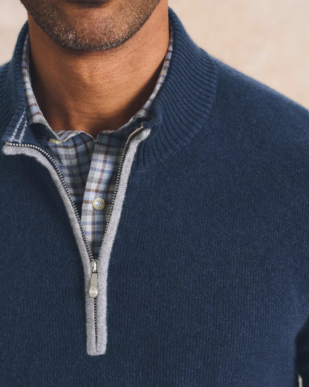 Close-up of a man wearing a navy blue quarter-zip knit sweater over a blue and white plaid button-down shirt.