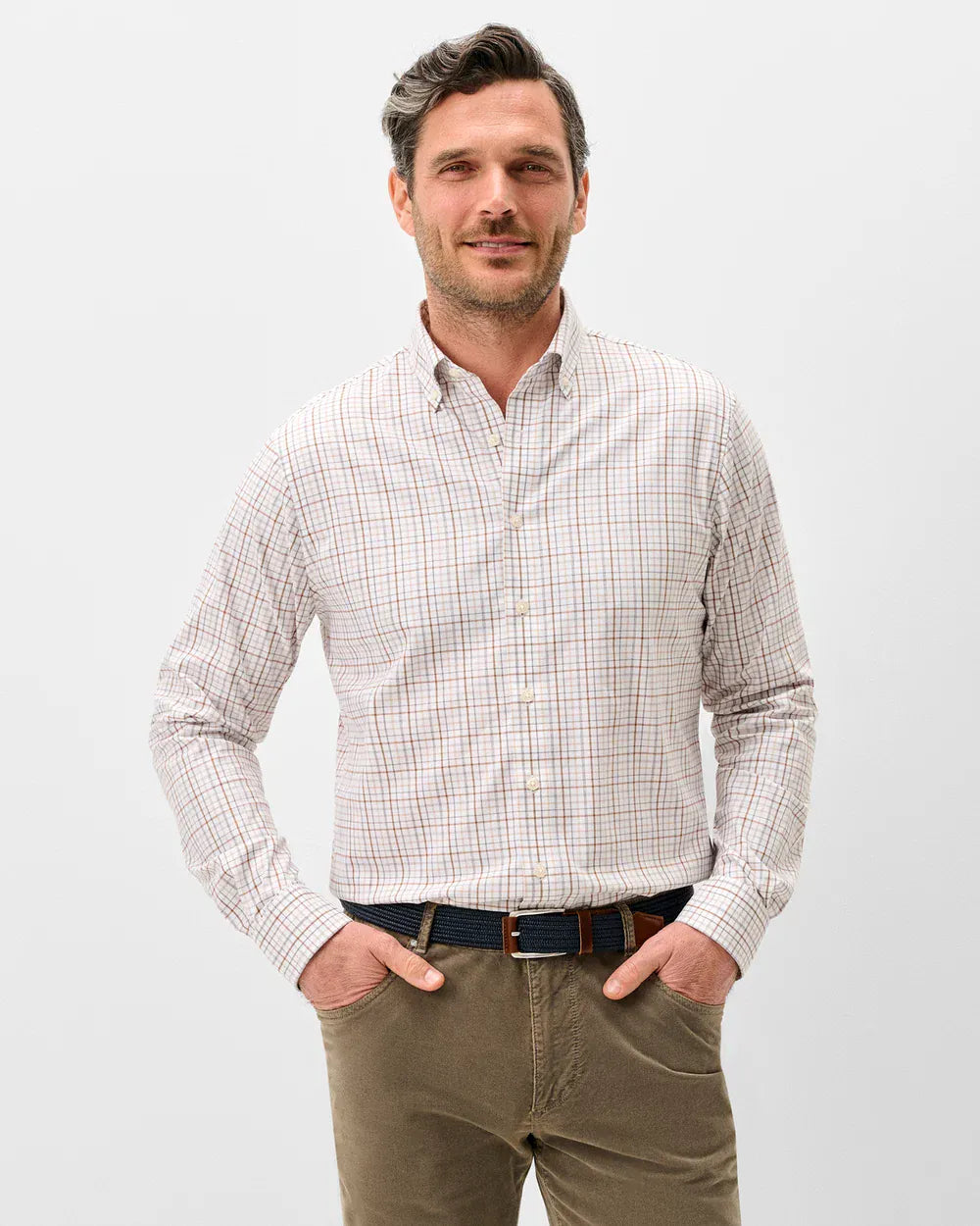 A man wearing a long-sleeve button-down shirt with a fine beige and brown checkered pattern, paired with olive green trousers and a dark belt, standing against a light gray background.