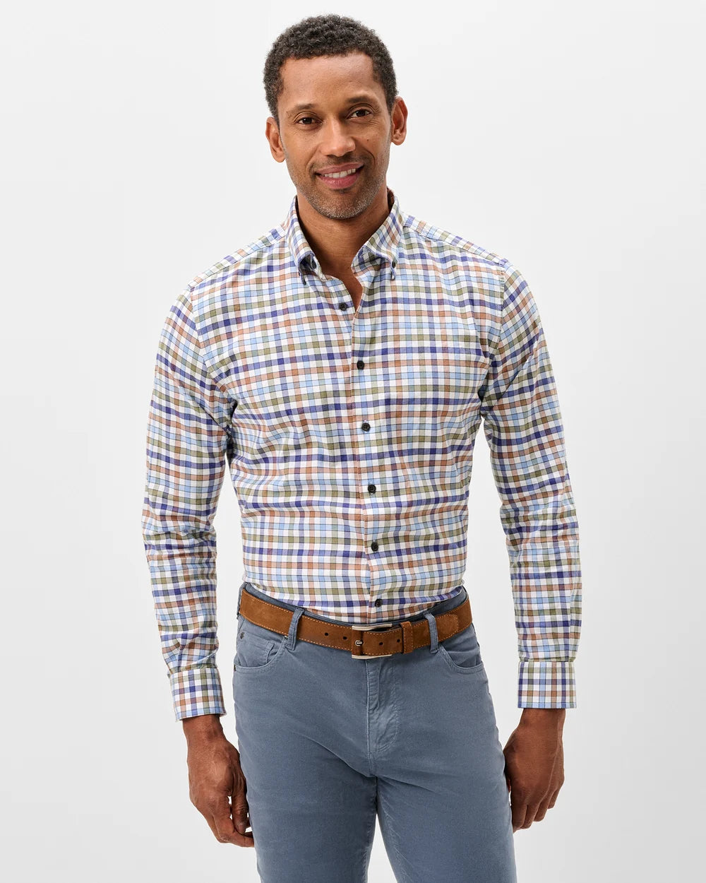 A man wearing a long-sleeve button-down shirt with a multicolor plaid pattern in blue, orange, and white, paired with blue jeans and a brown belt, against a plain light gray background.