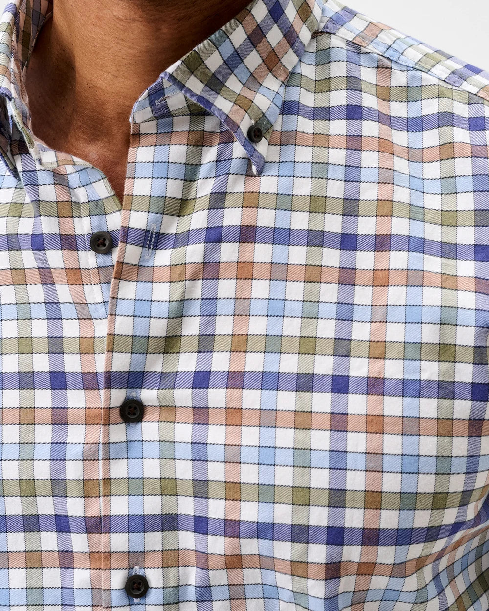 Close-up of a men's button-down shirt with a multicolor plaid pattern in blue, purple, green, and brown on a white base, worn by a model.