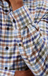 Close-up of a man wearing a long-sleeve plaid button-down shirt with a blue, brown, and white checkered pattern.