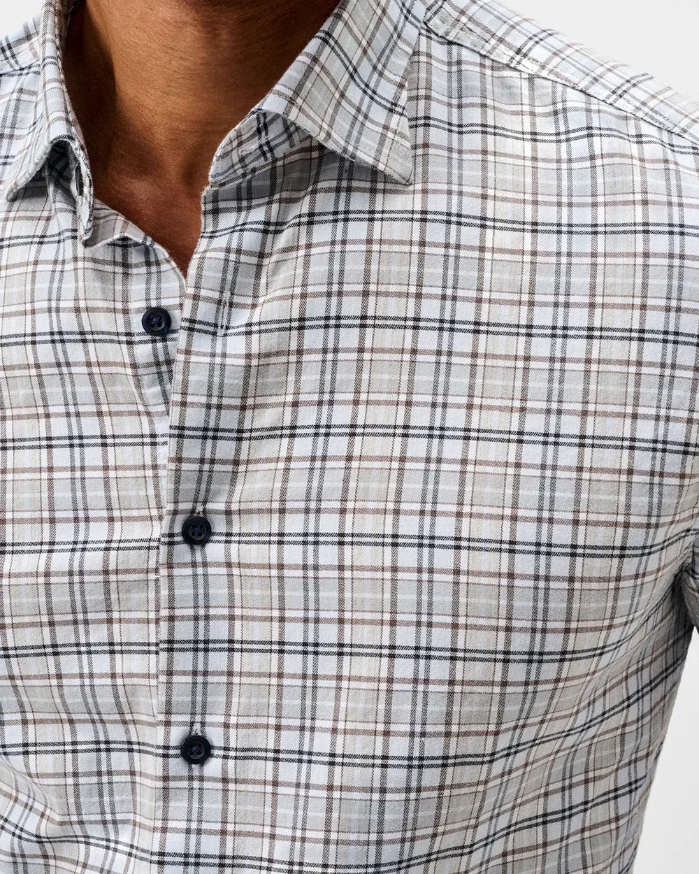 Close-up of a man wearing a long-sleeve plaid button-down shirt in beige, white, and brown with thin black lines.