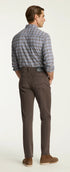 A man shown from the back wearing brown slim-fit trousers, a blue and gray plaid button-down shirt, and brown suede shoes, standing against a plain off-white studio background.