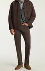 A man modeling a dark brown quilted overshirt jacket over a blue and white plaid shirt, gray vest, brown trousers, and brown suede shoes, photographed against a plain light gray studio background.