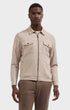 A man wearing a beige textured zip-up jacket with a collar and two chest pockets, paired with brown trousers, against a light gray studio background.