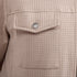 Close-up of a textured tweed jacket in a light beige or dusty rose color, featuring a pocket with a silver-tone metal snap button.