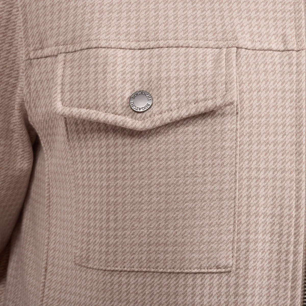 Close-up of a textured tweed jacket in a light beige or dusty rose color, featuring a pocket with a silver-tone metal snap button.