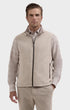 A man wearing a light beige zip-up vest over a beige plaid long-sleeve shirt and matching beige pants, photographed against a light gray studio background.