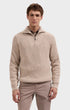 A man wearing a beige ribbed knit quarter-zip sweater with a stand collar, paired with light brown trousers, photographed against a solid light gray background.