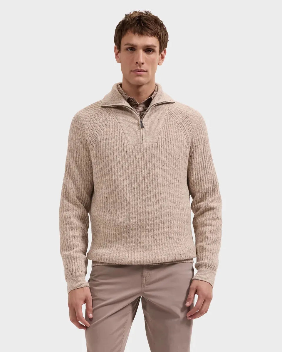 A man wearing a beige ribbed knit quarter-zip sweater with a stand collar, paired with light brown trousers, photographed against a solid light gray background.