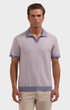 A man wearing a short-sleeve knit polo shirt in a light lavender-gray color with contrasting dusty blue trim on the collar, sleeve cuffs, and hem, paired with beige trousers, against a solid light gray background.