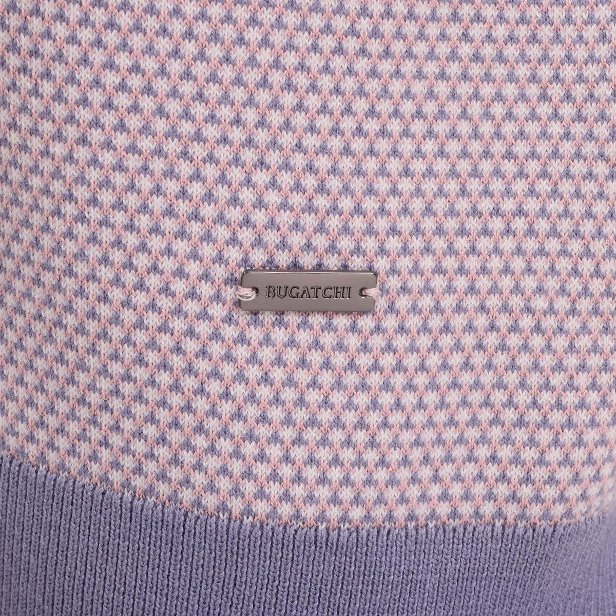 Close-up of a Bugatchi knit sweater featuring a fine pink and lavender-blue houndstooth pattern with a solid lavender ribbed hem and a silver-tone metal brand plaque.