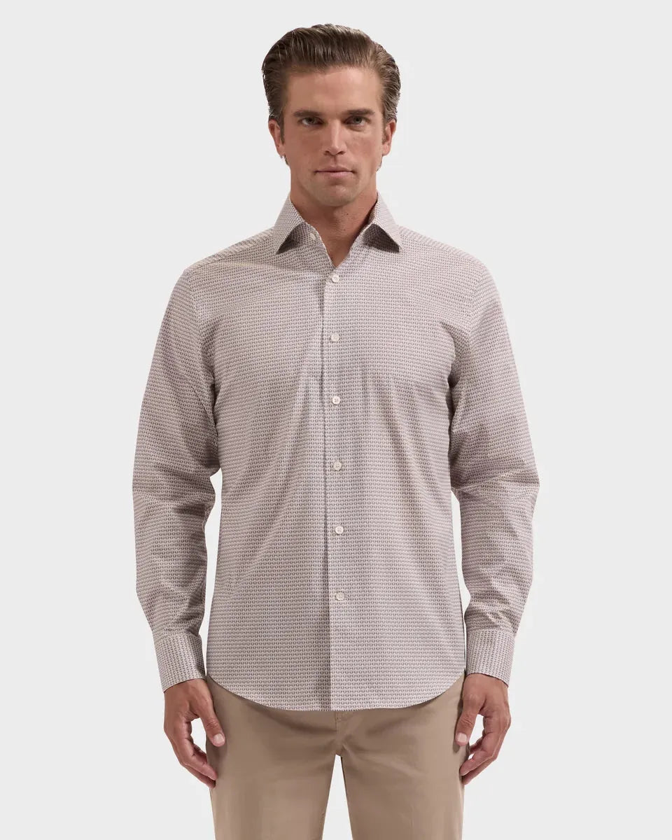 A man wearing a long-sleeve button-down dress shirt with a fine micro-pattern in beige and white, paired with khaki pants, against a light gray studio background.
