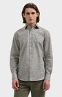 A man wearing a long-sleeve button-up shirt with a dense micro-pattern in black, white, and gray, paired with olive green trousers, shot against a solid light gray background.