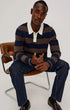 Man sitting on a chair wearing a striped sweater and dark jeans.