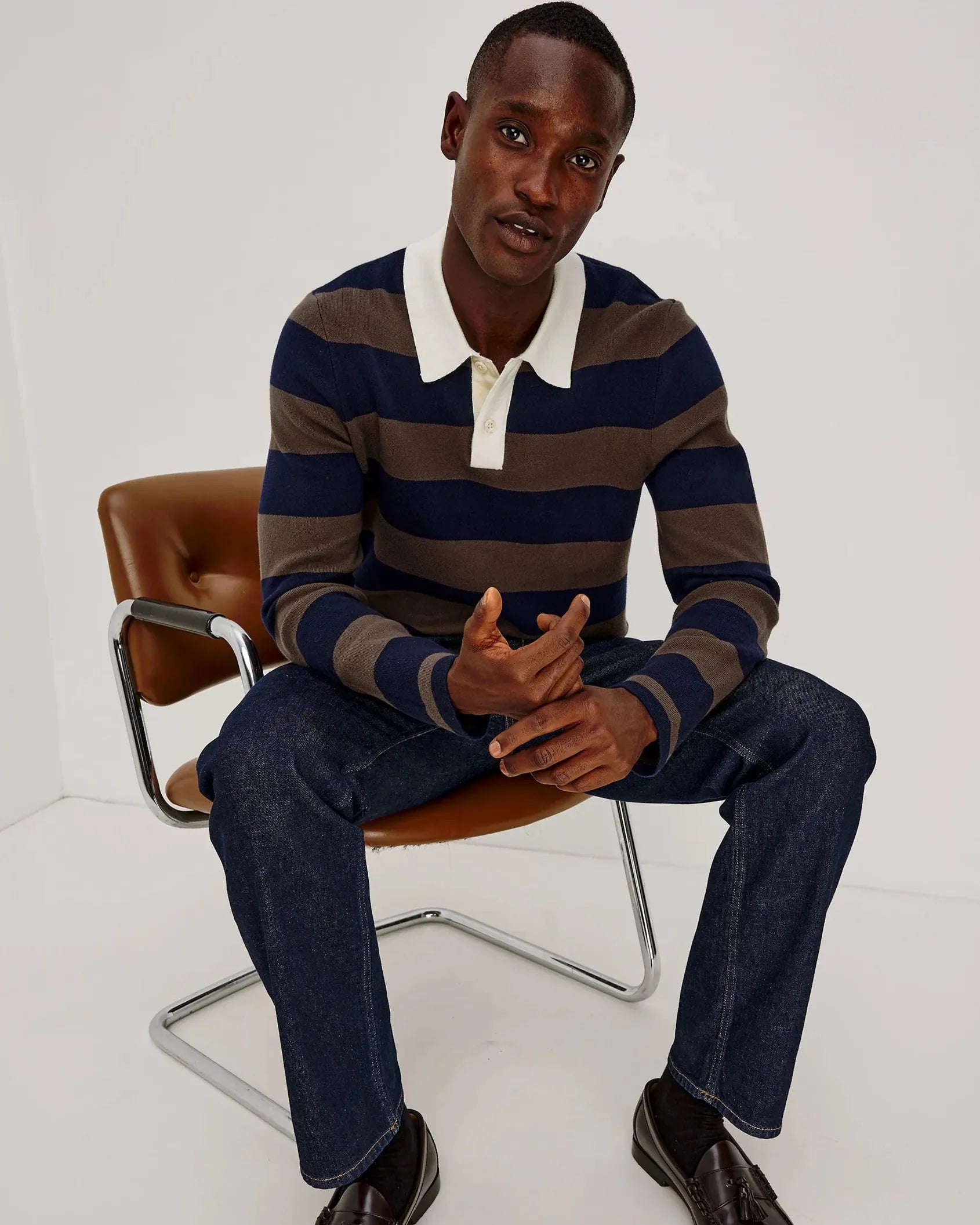 Man sitting on a chair wearing a striped sweater and dark jeans.