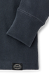 Close-up of a dark slate blue textured fleece sweatshirt showing the ribbed cuff and a black circular Filson brand patch near the hem.