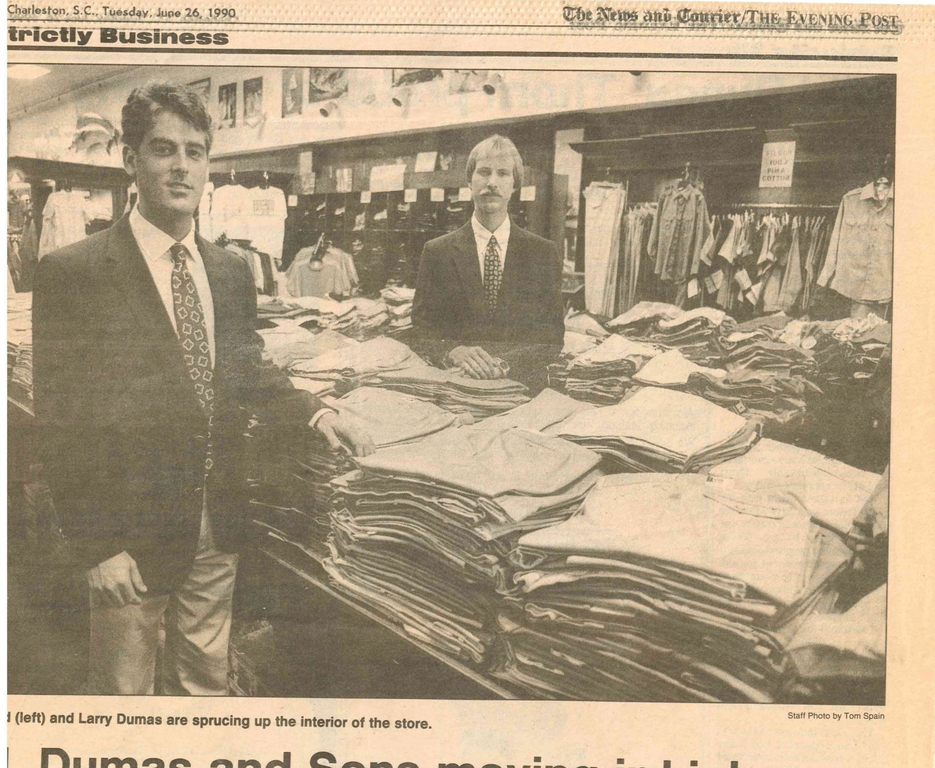 A scanned vintage newspaper page featuring a photo of a clothing store interior with stacks of folded garments and two men in suits, with visible masthead text and a date of June 25, 1992.