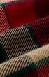 A close-up of a classic tartan plaid fabric with red, beige, black, and green stripes woven in a diagonal pattern.